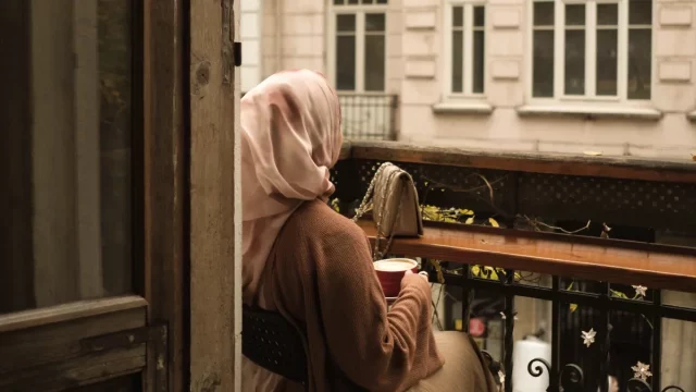 Seorang perempuan menikmati waktu sendiri di balkon sambil memandang kota.