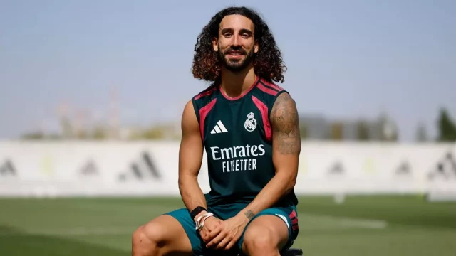 Marc Cucurella mengenakan kaus latihan Real Madrid dan duduk di tepi lapangan sambil tersenyum