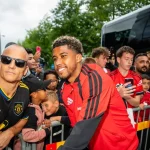Pemain Manchester United berjaket merah berfoto bersama suporter di balik pagar pembatas di dekat bus tim