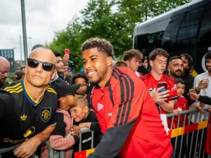 Pemain Manchester United berjaket merah berfoto bersama suporter di balik pagar pembatas di dekat bus tim