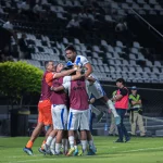 Sekelompok pemain sepak bola berpelukan merayakan gol di tepi lapangan sebuah stadion
