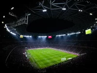 Ilustrasi pertandingan sepak bola malam hari yang disaksikan penonton di stadion.