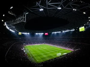Ilustrasi pertandingan sepak bola malam hari yang disaksikan penonton di stadion.