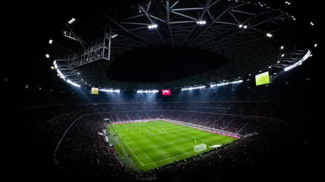Ilustrasi pertandingan sepak bola malam hari yang disaksikan penonton di stadion.