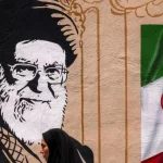 Seorang perempuan melintas di depan mural bergambar Ayatollah Ali Khamenei dan bendera Iran di Teheran