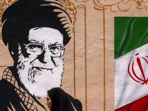 Seorang perempuan melintas di depan mural bergambar Ayatollah Ali Khamenei dan bendera Iran di Teheran