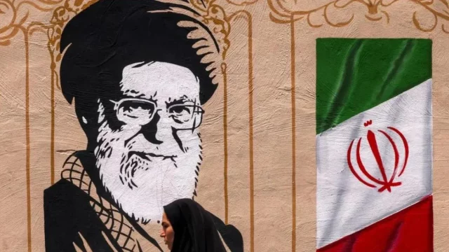 Seorang perempuan melintas di depan mural bergambar Ayatollah Ali Khamenei dan bendera Iran di Teheran