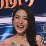 Natasha Wilona tertawa sambil mengangkat dua piala penghargaan di atas panggung