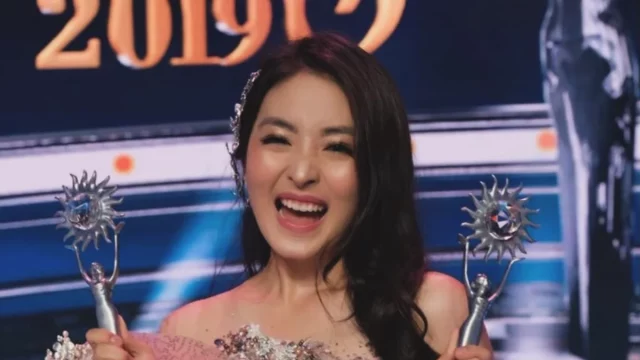 Natasha Wilona tertawa sambil mengangkat dua piala penghargaan di atas panggung