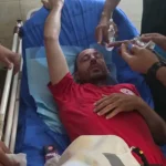 Seorang paramedis berseragam merah berbaring di brankar rumah sakit sambil mendapat penanganan pada matanya
