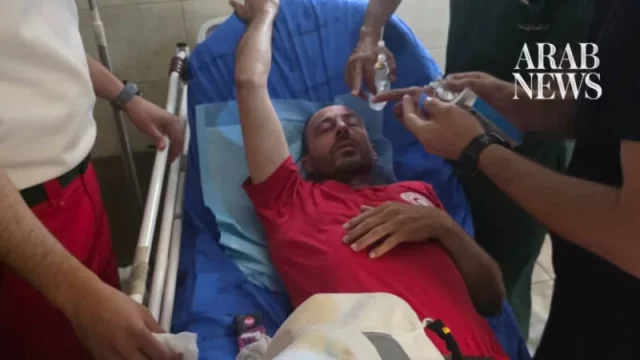 Seorang paramedis berseragam merah berbaring di brankar rumah sakit sambil mendapat penanganan pada matanya
