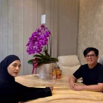 Paula Verhoeven berjilbab hitam duduk di meja bersama seorang tenaga medis