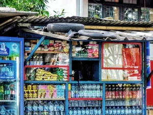 Warung kelontong kecil di pinggir jalan dengan aneka barang dagangan tertata di raknya