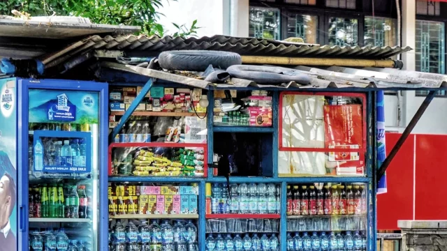 Warung kelontong kecil di pinggir jalan dengan aneka barang dagangan tertata di raknya
