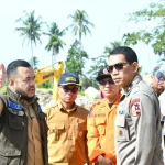 Sejumlah petugas berseragam meninjau kawasan sungai berbatu yang terdampak banjir dengan alat berat di latar belakang