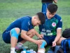 Ilustrasi dua pemain sepak bola muda memasang plester kinesiologi pada lutut dan pergelangan kaki di tepi lapangan