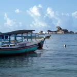 Perahu nelayan kayu tradisional berlabuh di laut tenang dengan gugusan batu granit dan pulau kecil di kejauhan