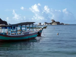 Perahu nelayan kayu tradisional berlabuh di laut tenang dengan gugusan batu granit dan pulau kecil di kejauhan