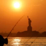 Siluet Patung Liberty berlatar langit jingga saat matahari terbenam di Pelabuhan New York