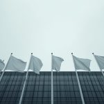 Ilustrasi deretan tiang bendera negara-negara Eropa di depan gedung kaca pemerintahan.