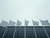 Ilustrasi deretan tiang bendera negara-negara Eropa di depan gedung kaca pemerintahan.