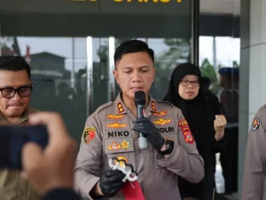Kapolres Garut berseragam cokelat berbicara di depan mikrofon sambil menunjukkan barang bukti senjata pukul