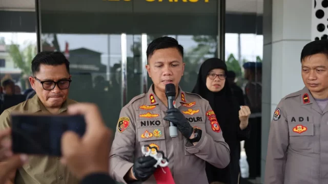 Kapolres Garut berseragam cokelat berbicara di depan mikrofon sambil menunjukkan barang bukti senjata pukul