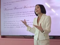 Prilly Latuconsina berjas krem berdiri di depan layar presentasi berlatar merah muda