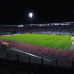 Ilustrasi stadion sepak bola dengan lampu menyala pada malam hari.
