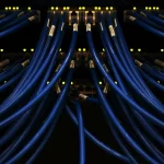 Deretan kabel jaringan biru terhubung ke perangkat di ruang server pusat data