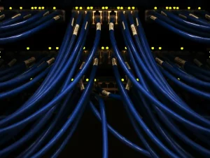Deretan kabel jaringan biru terhubung ke perangkat di ruang server pusat data