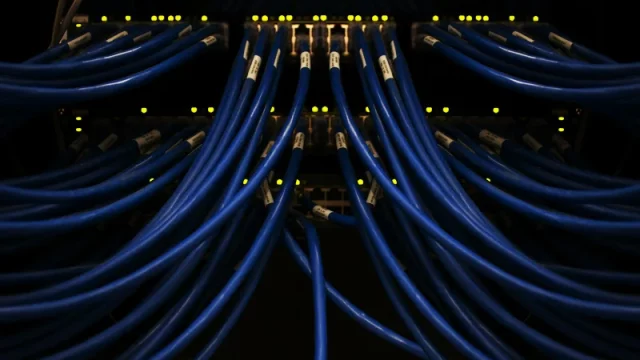 Deretan kabel jaringan biru terhubung ke perangkat di ruang server pusat data