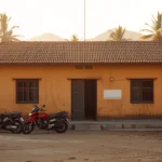 Bangunan puskesmas satu lantai berdinding polos di kawasan perdesaan dengan beberapa sepeda motor terparkir di halamannya