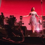 Raisa bernyanyi di atas panggung The Sounds Project mengenakan gaun lavender dengan latar layar besar dan lampu panggung merah
