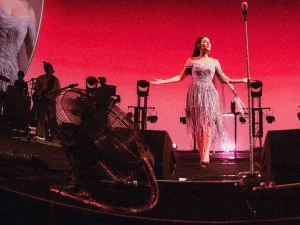 Raisa bernyanyi di atas panggung The Sounds Project mengenakan gaun lavender dengan latar layar besar dan lampu panggung merah