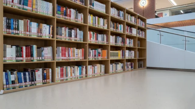 Deretan rak kayu berisi buku di sebuah perpustakaan universitas dengan lantai terang di depannya