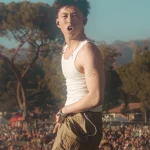Rich Brian bernyanyi di atas panggung festival musik dengan kerumunan penonton di belakangnya