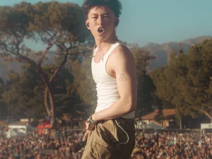 Rich Brian bernyanyi di atas panggung festival musik dengan kerumunan penonton di belakangnya