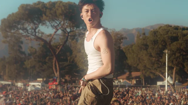 Rich Brian bernyanyi di atas panggung festival musik dengan kerumunan penonton di belakangnya