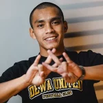 Ripal Wahyudi mengenakan kaus hitam bertuliskan Dewa United sambil membentuk simbol dengan kedua tangannya