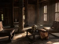 Ilustrasi ruang tamu rumah panggung kayu adat dengan tiang berukir, lantai tikar anyaman, dua kursi rendah berhadapan, dan meja pendek berisi wadah sirih kuningan, cangkir keramik, serta kain terlipat