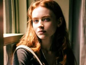 Potret Sadie Sink dengan rambut merah menyala duduk di dekat jendela