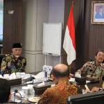 Sejumlah pejabat duduk mengelilingi meja rapat di ruang pertemuan kementerian dengan bendera Merah Putih dan lambang Garuda di dinding