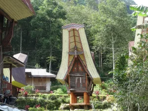 Rumah adat tongkonan dan lumbung padi Toraja dengan dinding berukir geometris berwarna merah, hitam, putih, dan kuning di lereng berhutan