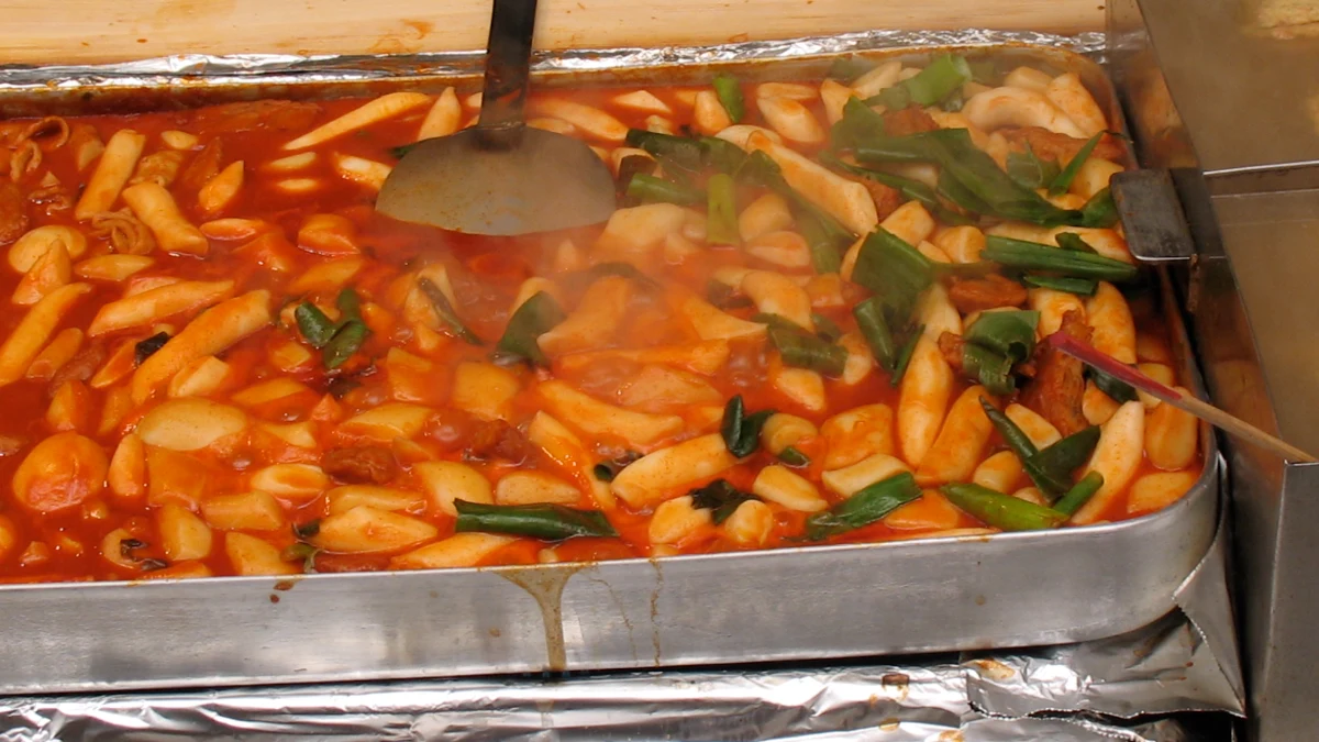 Tteokbokki berkuah merah pedas di wadah pemanas jajanan jalanan.