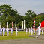 Ilustrasi upacara pengibaran bendera oleh petugas berseragam.