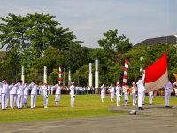 Ilustrasi upacara pengibaran bendera oleh petugas berseragam.