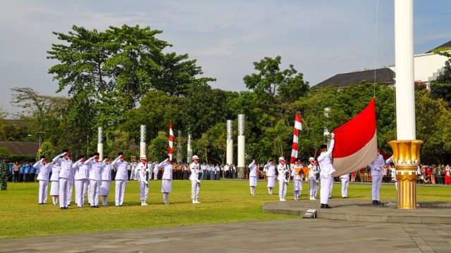 Ilustrasi upacara pengibaran bendera oleh petugas berseragam.