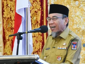 Seorang pejabat berseragam dinas berbicara di depan mikrofon dengan latar kain bermotif emas