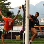 Ilustrasi dua pemain sepak takraw melompat berebut bola di dekat tiang net di Visayas State University, Filipina